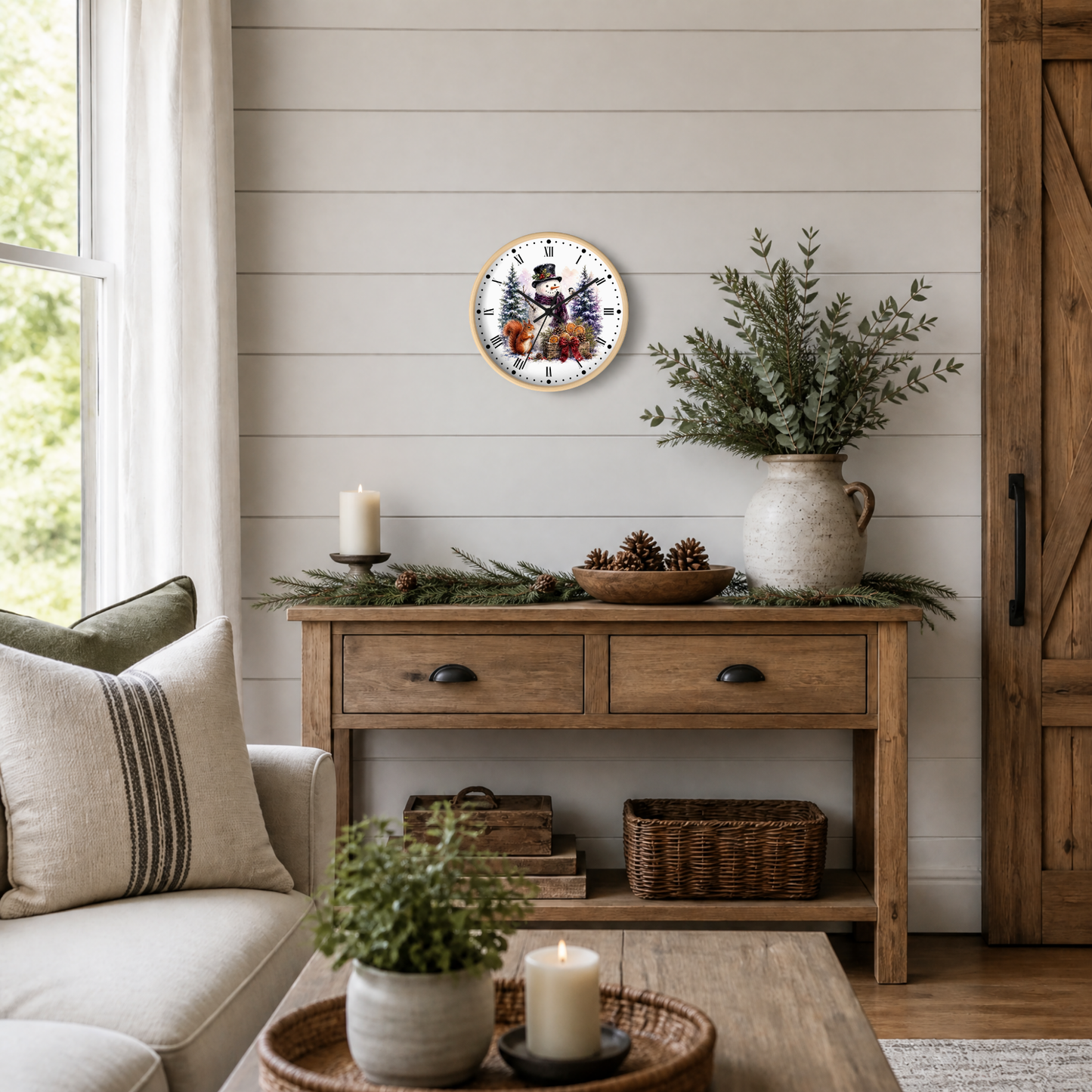 A round wall clock featuring a festive snowman and squirrel illustration, styled in a cozy, rustic living room setting above a wooden console table with holiday greenery and candles.