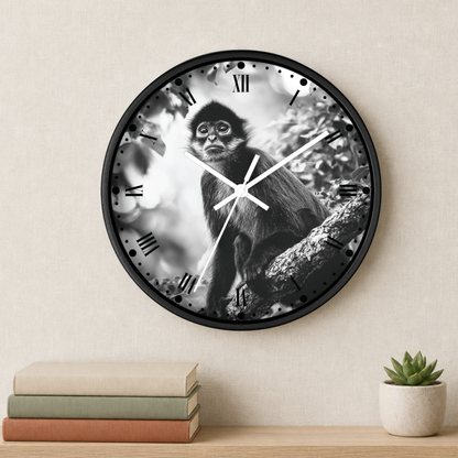 A round wall clock with a black frame and a monochrome photograph of a monkey on the clock face, styled on a beige wall above a shelf with books and a small plant.