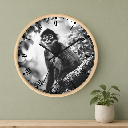 A round wall clock with a light wood frame hangs on a sage green wall above a wooden shelf. The clock face features a black and white photograph of a monkey sitting on a tree branch.