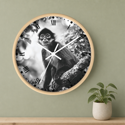 Round wall clock with a light wood frame, featuring a black and white photograph of a monkey on the clock face with Roman numerals, mounted on a sage green wall above a wooden shelf with a small potted plant.