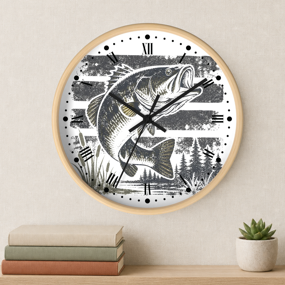 A round wall clock with a light wood frame and a white face featuring a black-and-gray fish and forest illustration. The clock is mounted on a beige wall above a shelf with stacked books and a small potted succulent.