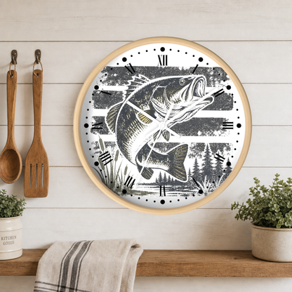 Round wall clock with a light wood frame featuring a black and white illustration of a largemouth bass over a striped rustic background. The clock is mounted on a white wood paneled wall above a wooden shelf with a striped towel, potted plants, and hanging wooden kitchen utensils.