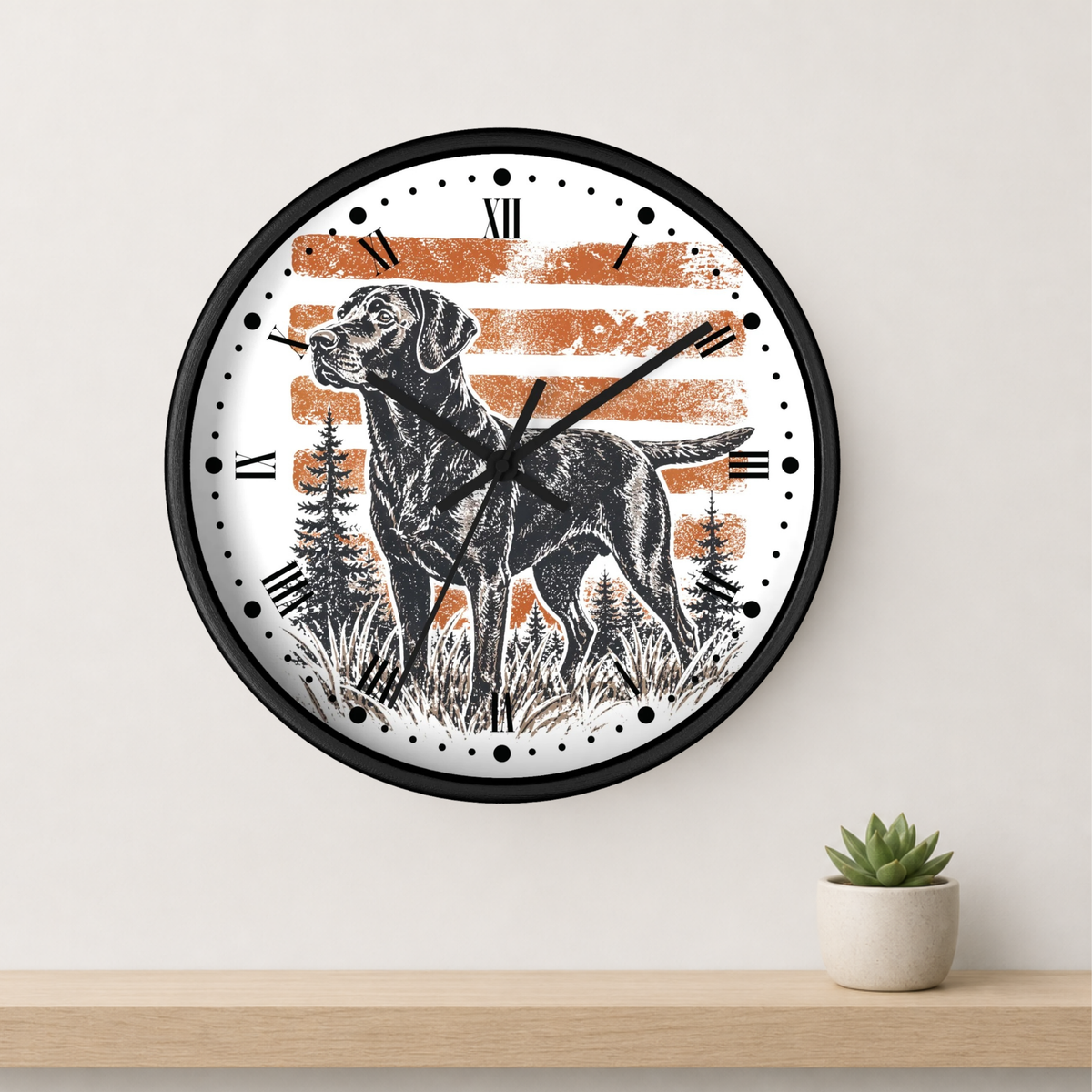 A round wall clock with a black frame and a white face featuring a black Labrador retriever illustration, black Roman numerals, and distressed orange horizontal stripes. The clock is mounted on a light beige wall above a light wood shelf with a small potted succulent.
