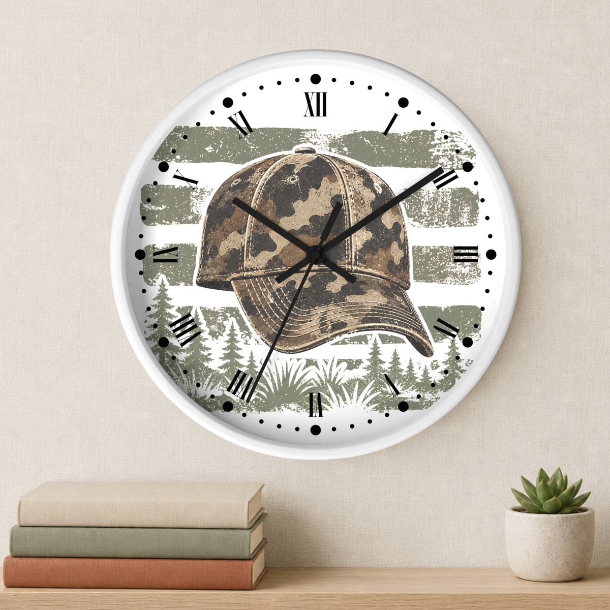 A round wall clock with a white frame and a printed design featuring a camouflage baseball cap over a distressed tree-flag background and pine forest. The clock is mounted on a beige wall above a wooden shelf with stacked books and a small potted succulent.