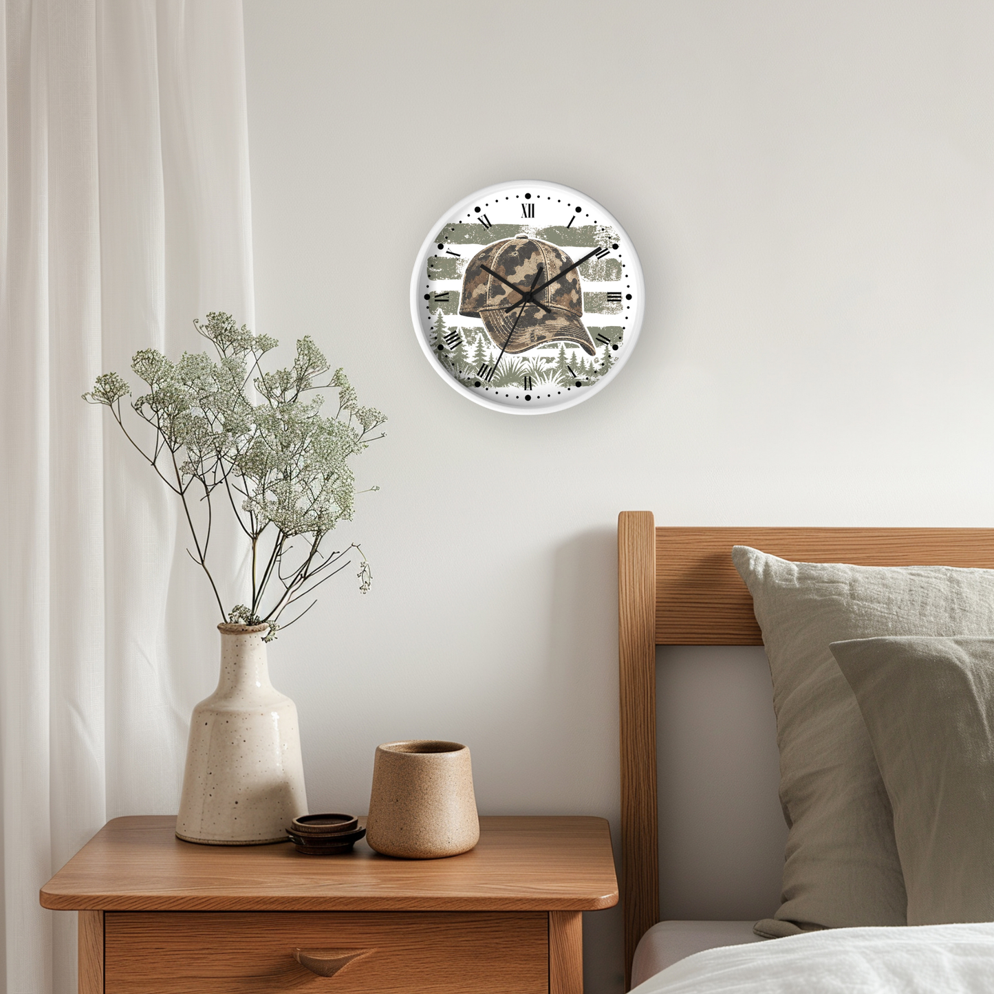 A round wall clock with a camouflage-patterned face and white rim, hanging on a light gray wall above a wooden nightstand with a vase of dried flowers and a bed with pillows.