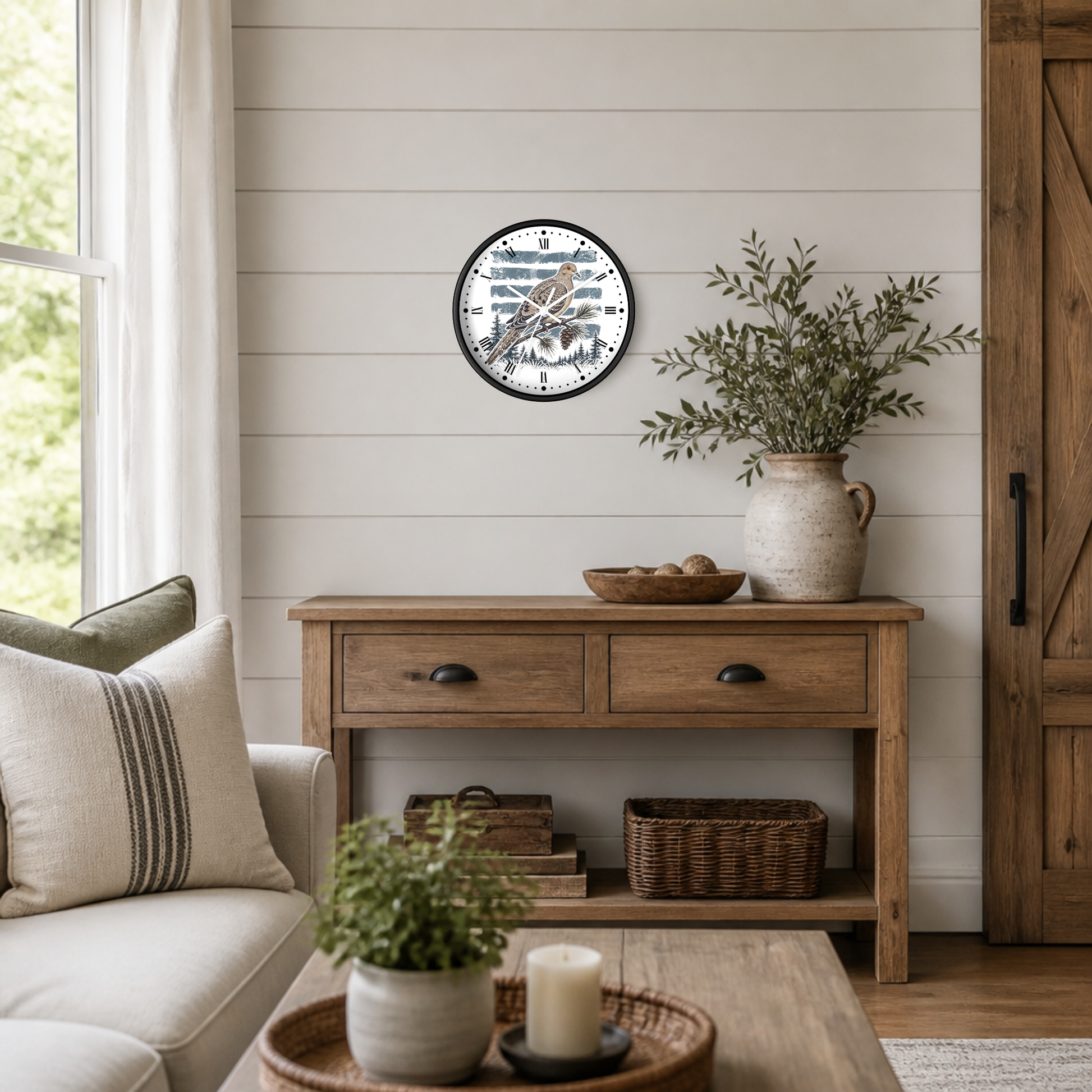 A round wall clock with a black frame and a white face featuring a brown dove bird illustration, styled on a white shiplap wall above a rustic wooden console table in a bright, modern farmhouse living room.