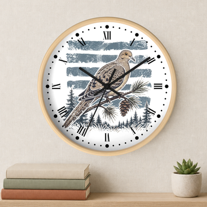 A round wall clock with a light wood frame hangs on a beige wall above a shelf with stacked books and a small potted succulent. The clock face features a detailed illustration of a brown dove bird perched on a pine branch with a pinecone, set against a background of blue-gray horizontal stripes and a dark pine forest silhouette.