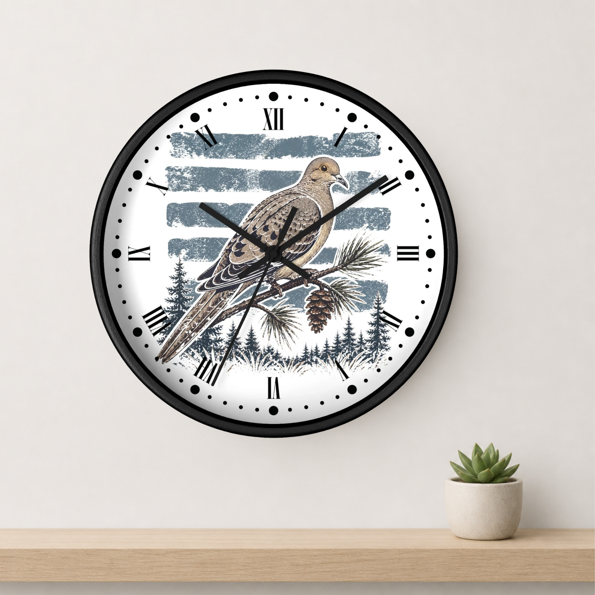 A round wall clock with a black frame and a white face featuring a dove bird perched on a pine branch against blue-gray brushstroke stripes and a dark forest silhouette. The clock hangs on a light wall above a wooden shelf with a small potted succulent.