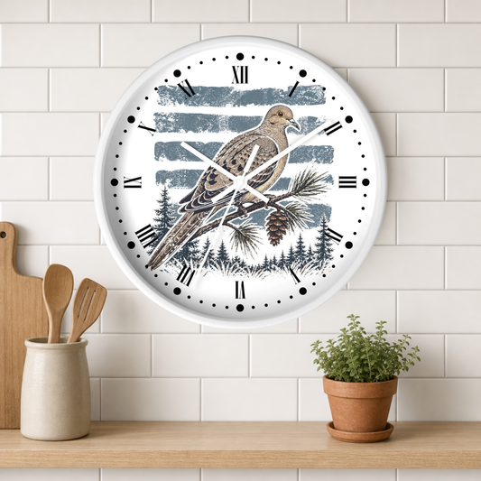 A round wall clock with a white face and black Roman numerals, featuring an illustration of a brown dove bird perched on a pine branch against blue-gray striped and forest backgrounds. The clock is mounted on a white subway tile wall above a wooden shelf with a small potted plant and wooden utensils.