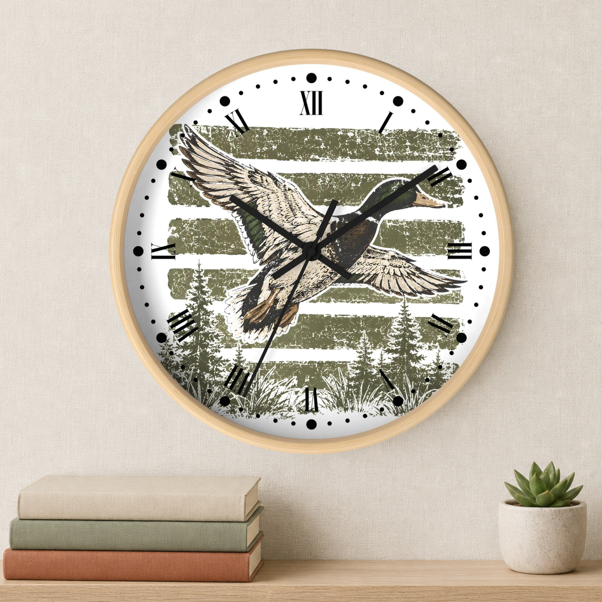 A round wall clock with a light wood frame hangs on a beige wall above a shelf with stacked books and a small potted succulent. The clock face features a rustic green and white striped background with a detailed illustration of a flying duck.