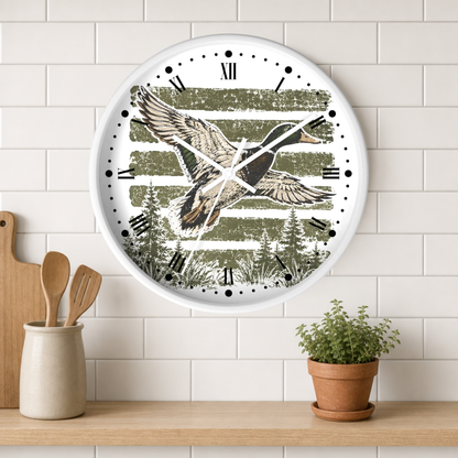 A round wall clock with a white frame hangs on a white subway tile wall above a wooden shelf. The clock face features a rustic green and white striped background with an illustration of a flying duck and pine trees.