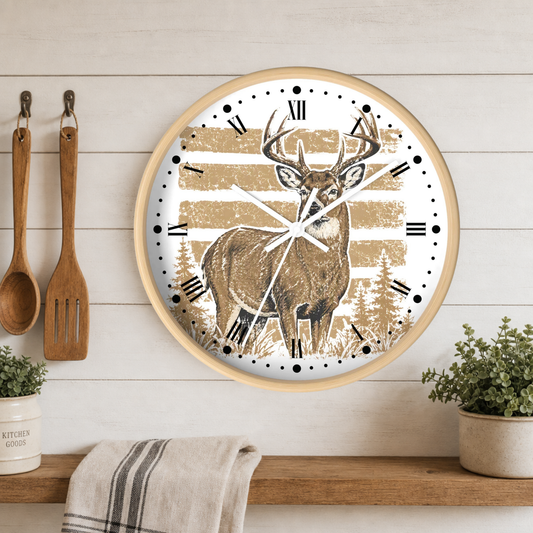 Round wall clock with a light wood frame, featuring a deer illustration over tan and white horizontal stripes with black Roman numerals. The clock is mounted on a white wood-paneled wall above a wooden shelf with kitchen utensils, plants, and a towel.