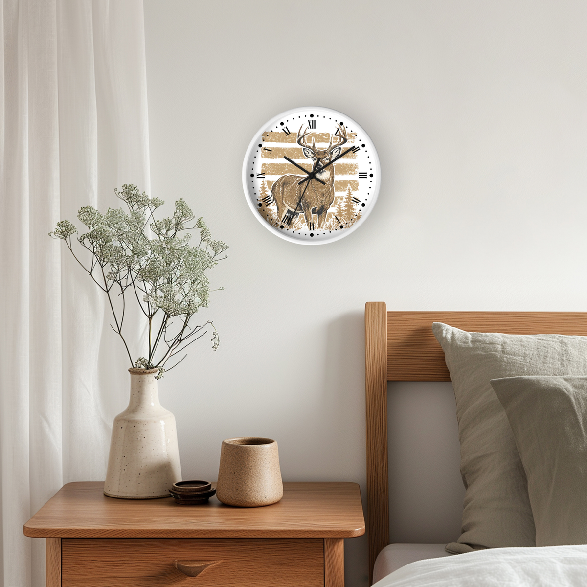 A round wall clock with a white frame and a printed deer illustration hangs on a light gray bedroom wall above a wooden nightstand with a vase and candles, next to a bed with pillows.