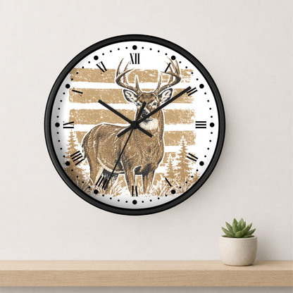 A round wall clock with a black frame and a rustic deer illustration on the face, mounted on a light beige wall above a wooden shelf with a small potted succulent.