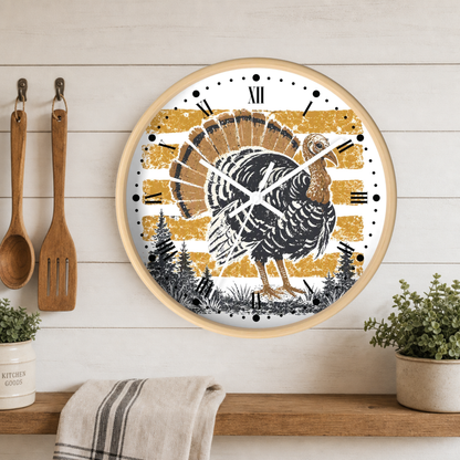 A round wall clock with a rustic Thanksgiving turkey design, featuring a black and white turkey on a distressed gold and white striped background. The clock has a light wood frame and is mounted on a white wood-paneled wall above a wooden shelf with kitchen utensils and plants.