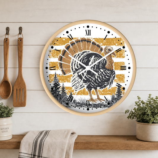 A round wall clock with a rustic Thanksgiving turkey design, featuring a black and white turkey on a distressed gold and white striped background. The clock has a light wood frame and is mounted on a white wood-paneled wall above a wooden shelf with kitchen utensils and plants.