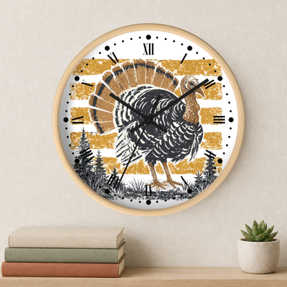 A round wall clock with a light wood frame hangs on a beige wall above a shelf with stacked books and a small succulent. The clock face features a large black and brown turkey silhouette over a distressed gold and white striped background, with black Roman numerals and clock hands.