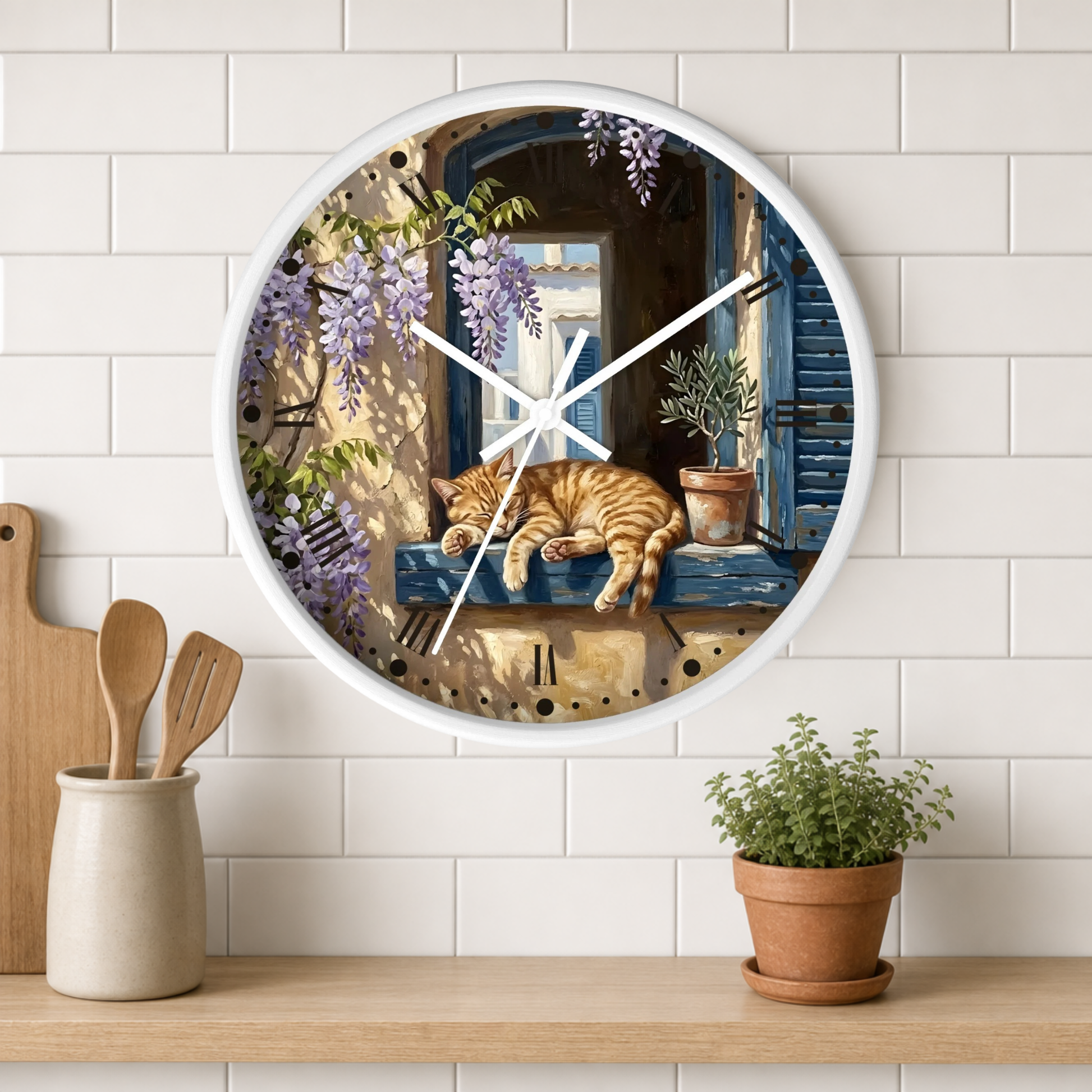 Round wall clock with a white frame and a printed illustration of an orange tabby cat sleeping on a blue window sill under purple wisteria, mounted on a white subway tile wall above a wooden shelf with kitchen utensils and a potted plant.