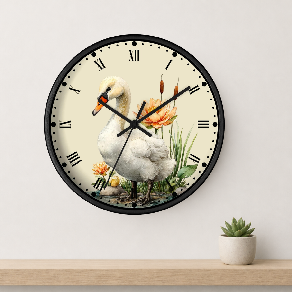 A round wall clock with a black frame and a cream-colored face featuring an illustration of a white swan, orange flowers, and green reeds. The clock is mounted on a light gray wall above a wooden shelf with a small potted succulent.