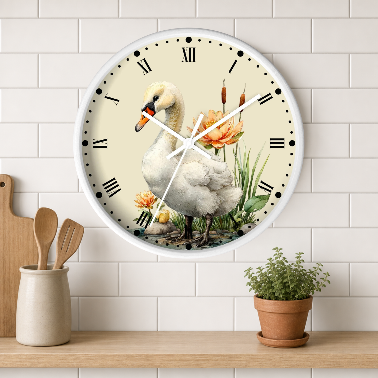 A round wall clock with a white frame and a vintage-style illustration of a white swan, orange flowers, and green reeds on the face, mounted on a white subway tile wall above a wooden shelf with a small potted plant and wooden utensils.