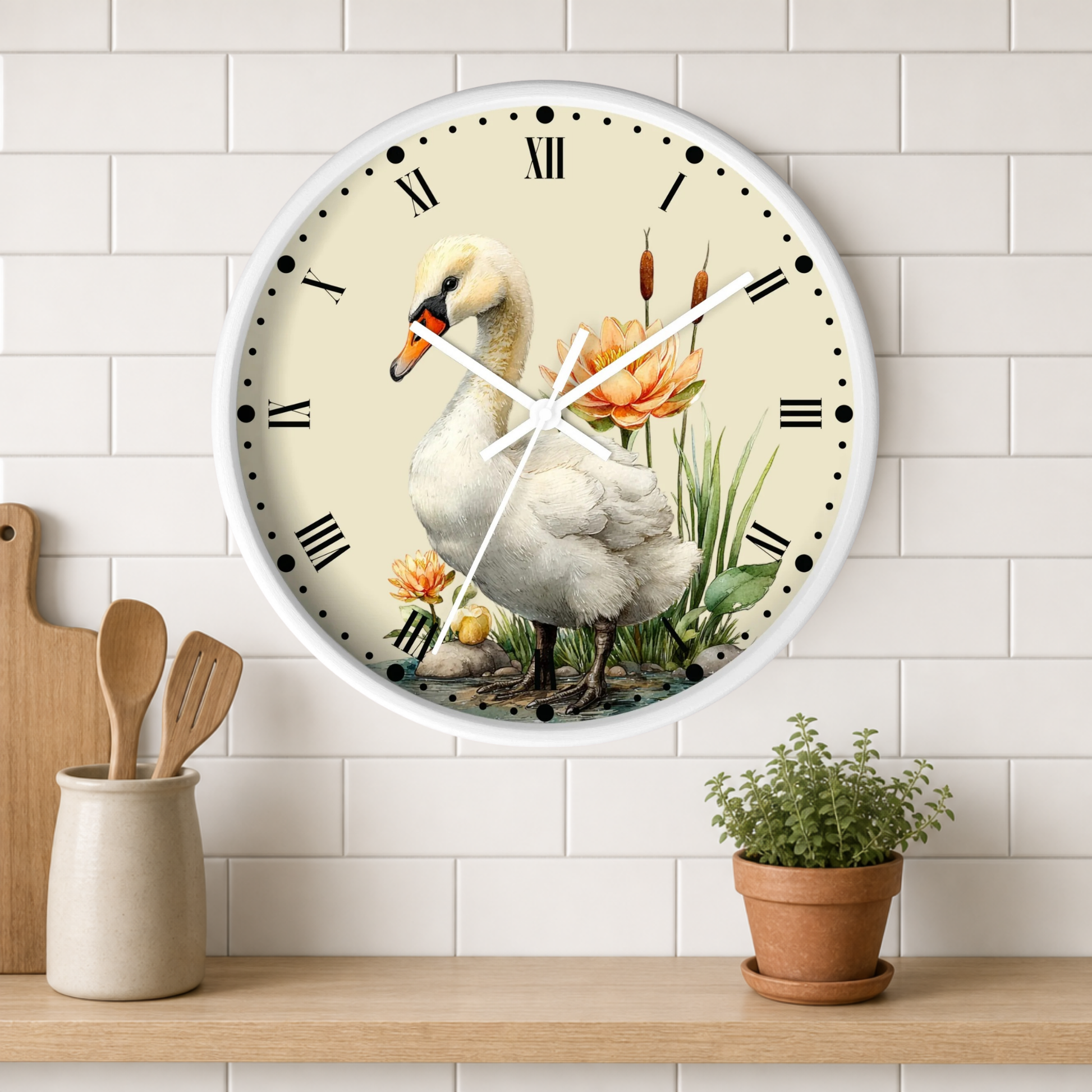 A round wall clock with a white frame and a vintage-style illustration of a white swan, orange flowers, and green reeds on the face, mounted on a white subway tile wall above a wooden shelf with a small potted plant and wooden utensils.