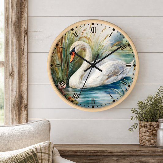 A round wall clock with a natural wood frame hangs on a white shiplap wall above a wooden table. The clock face features a painted white swan in blue water with green reeds, black Roman numerals, and black clock hands.