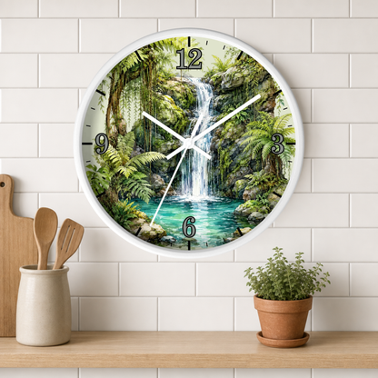A round wall clock with a white frame hangs on a white subway tile wall above a wooden shelf. The clock face features a detailed tropical jungle waterfall scene with green foliage, a white waterfall, and turquoise water.