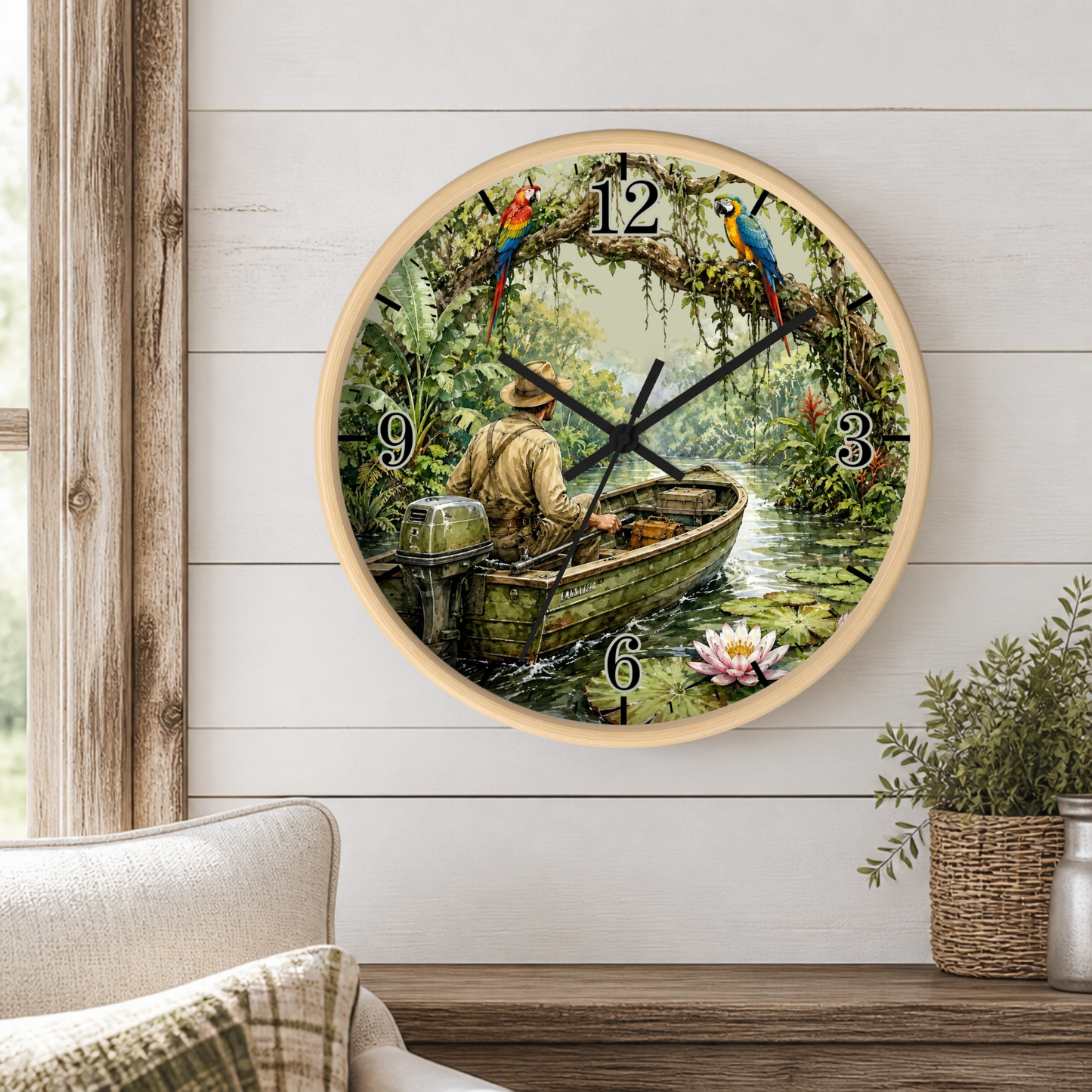 A round wall clock with a light wood frame hangs on a white shiplap wall above a wooden table. The clock face features a scenic illustration of a man rowing in a small boat on a river, surrounded by lush green foliage, colorful parrots, and a pink lotus flower.