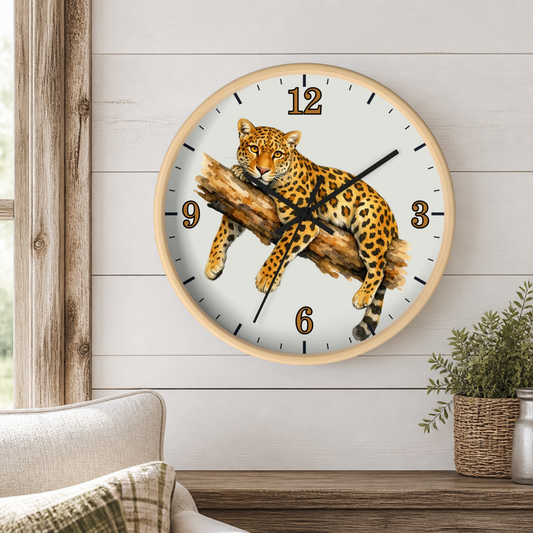 A round wall clock with a light wood frame and a white face featuring a detailed illustration of a leopard resting on a log. The clock is mounted on a white shiplap wall above a wooden mantel, with a sofa and a small potted plant visible in the room setting.
