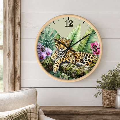 A round wall clock with a natural wood frame hangs on a white wood-paneled wall above a wooden shelf. The clock face features a detailed illustration of a leopard surrounded by tropical green leaves and pink flowers.