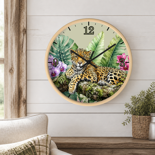 A round wall clock with a natural wood frame hangs on a white wood-paneled wall above a wooden shelf. The clock face features a detailed illustration of a leopard surrounded by tropical green leaves and pink flowers.