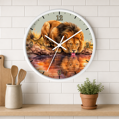 A round wall clock with a white frame and a printed lion drinking water design, mounted on a white subway tile wall above a wooden shelf with kitchen utensils and a small potted plant.