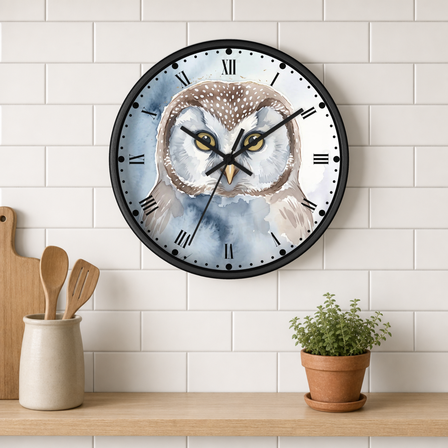 A round wall clock with a watercolor owl illustration on the face, mounted on a white subway tile wall above a wooden shelf with a small potted plant and wooden utensils.