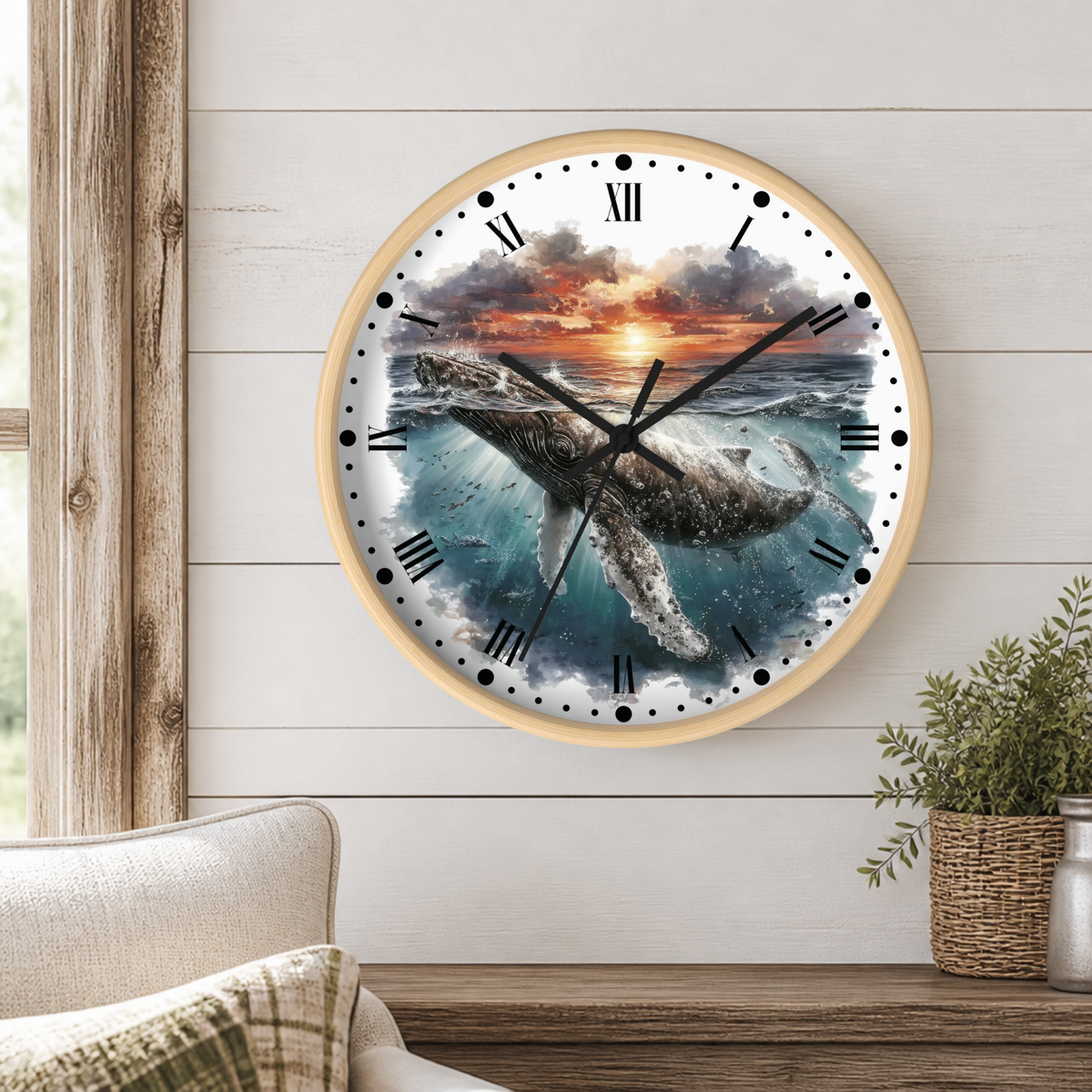 A round wall clock with a light wood frame hangs on a white shiplap wall above a wooden table. The clock face features a detailed illustration of a humpback whale swimming through blue ocean water under a dramatic sunset sky.