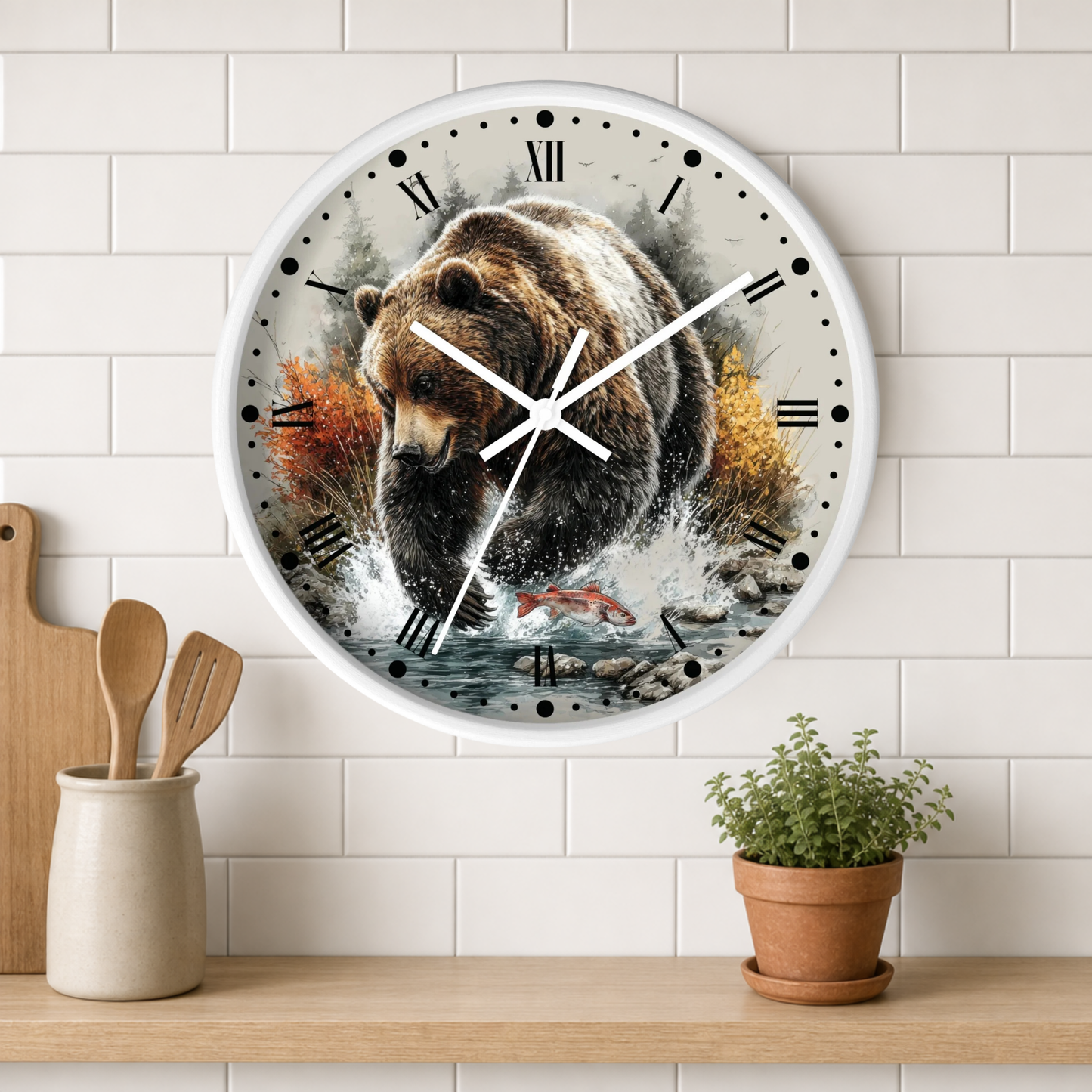 A round wall clock with a white frame and Roman numerals, featuring a detailed illustration of a brown bear walking through water with salmon, mounted on a white subway tile wall above a wooden shelf with a small plant and utensils.
