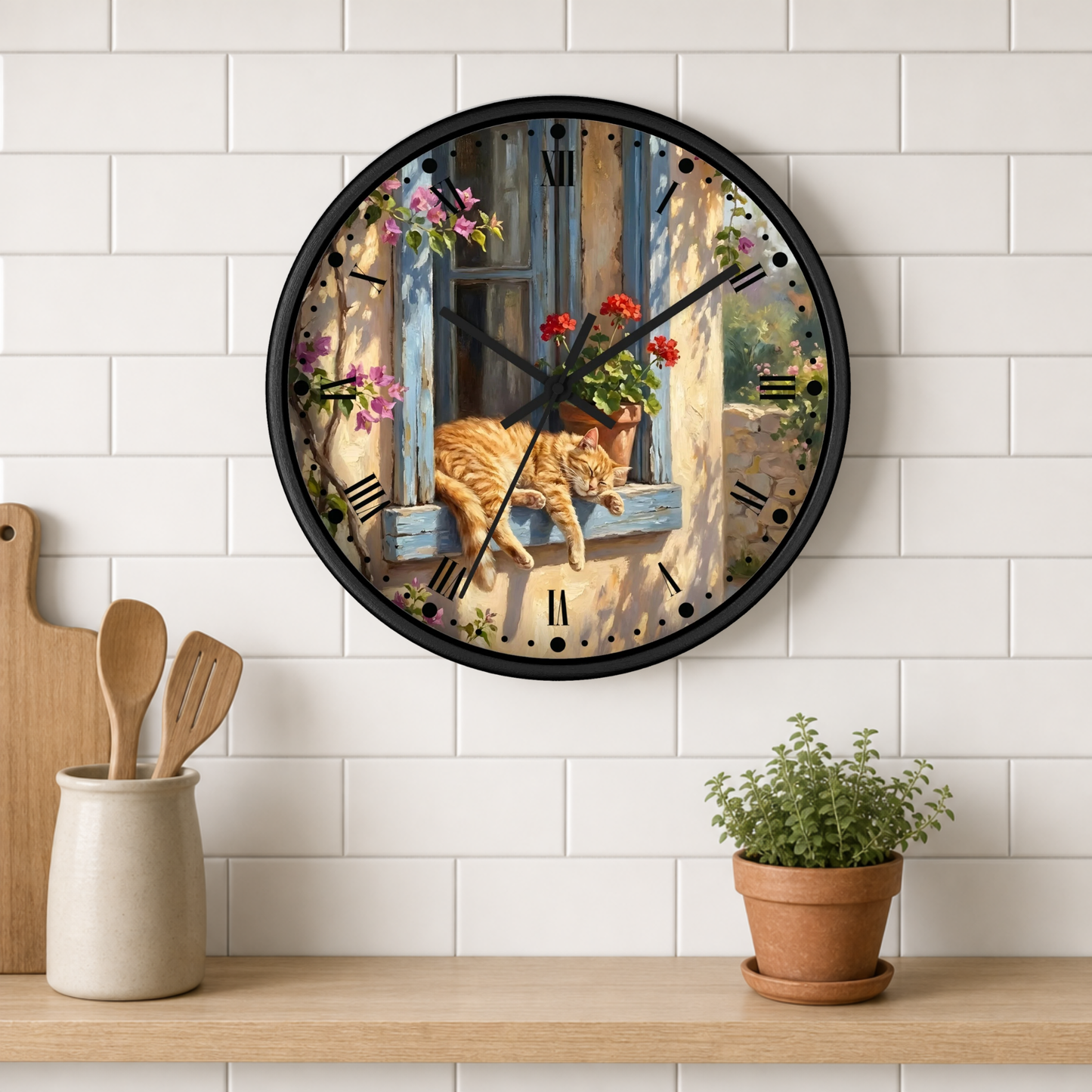 A round wall clock with a black frame hangs on a white subway-tile kitchen wall above a wooden shelf. The clock face features a scenic illustration of an orange tabby cat resting on a blue window sill with pink and red flowers, alongside a warm beige wall and soft shadows.