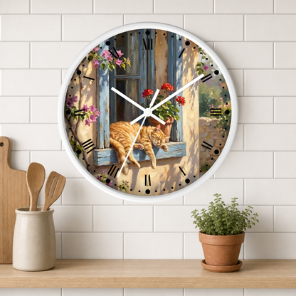 A round wall clock with a white frame hangs on a white subway tile wall above a wooden shelf. The clock face features a colorful illustration of an orange tabby cat lying on a blue window sill with pink and red flowers, set against a rustic sunlit wall.