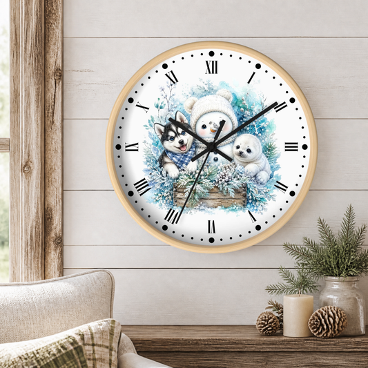 A round wall clock with a light wood frame hangs on a white shiplap wall above a wooden table. The clock face features a winter illustration of a snowman, a husky, a seal, and blue floral elements.