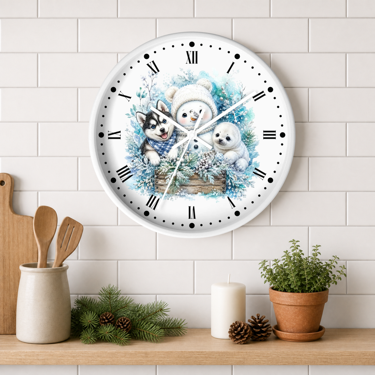 A round white wall clock with a winter illustration of a husky, snowman, and small seal, mounted on a white subway tile wall above a wooden shelf with kitchen decor and a potted plant.