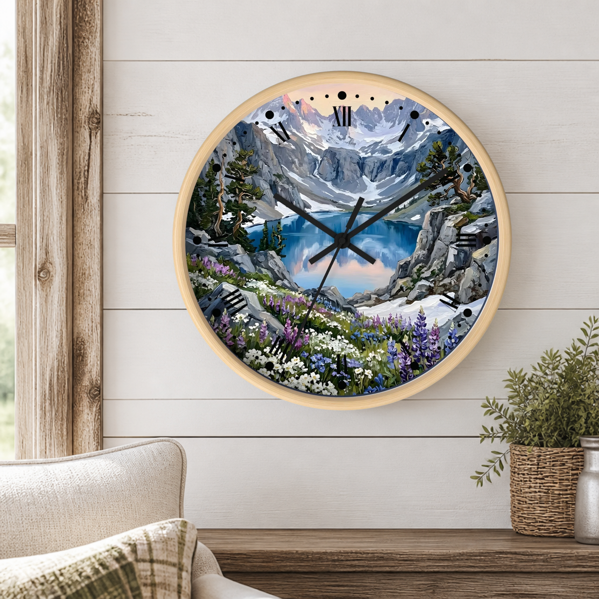 A round wall clock with a light wood frame and a scenic mountain landscape print, mounted on a white wood-paneled wall above a wooden shelf with a plant and part of a sofa visible.
