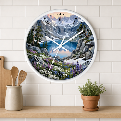 A round wall clock with a white frame and a scenic mountain landscape print, mounted on a white subway tile wall above a wooden shelf with kitchen utensils and a potted plant.
