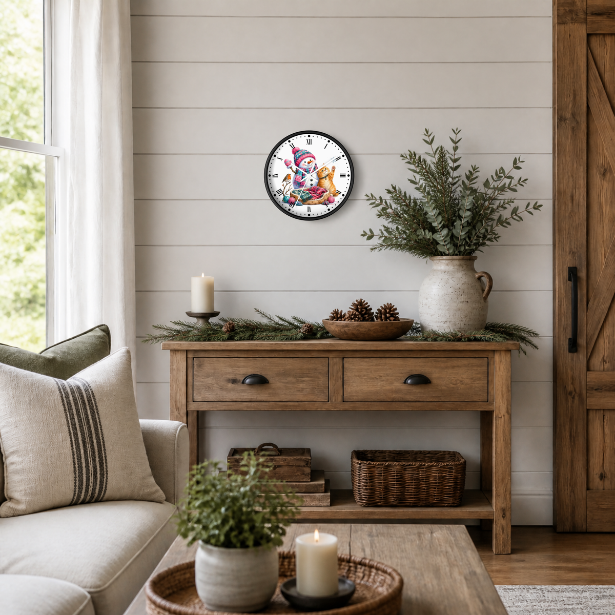 A round wall clock with a colorful snowman, ginger cat, and robin bird illustration and black numerals, styled on a shiplap wall above a rustic wooden console table in a cozy living room setting.