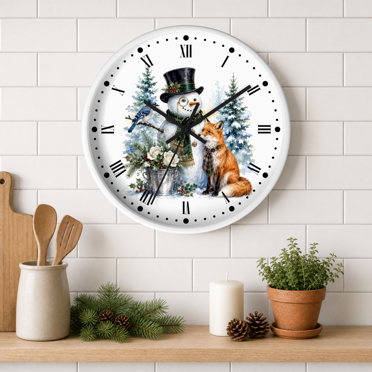 A round wall clock with a white face and black Roman numerals, decorated with a winter illustration of a snowman in a top hat and a red fox, hanging on a white subway tile wall above a shelf with kitchen props.