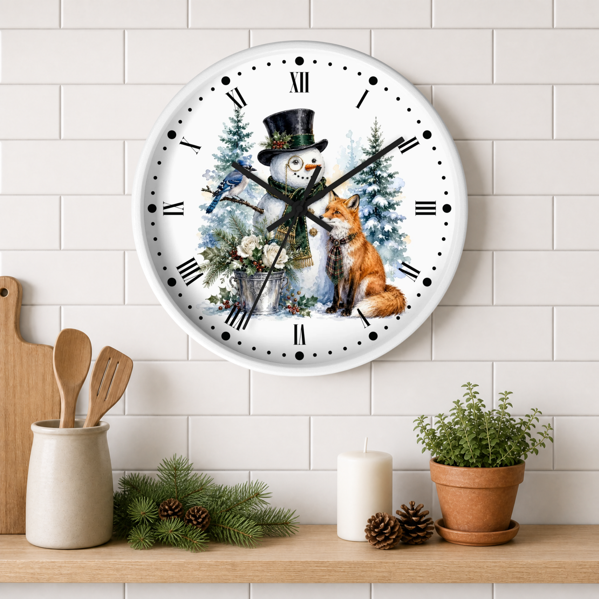 A round wall clock with a white face and black Roman numerals, decorated with a winter illustration of a snowman in a top hat and a red fox, hanging on a white subway tile wall above a shelf with kitchen props.