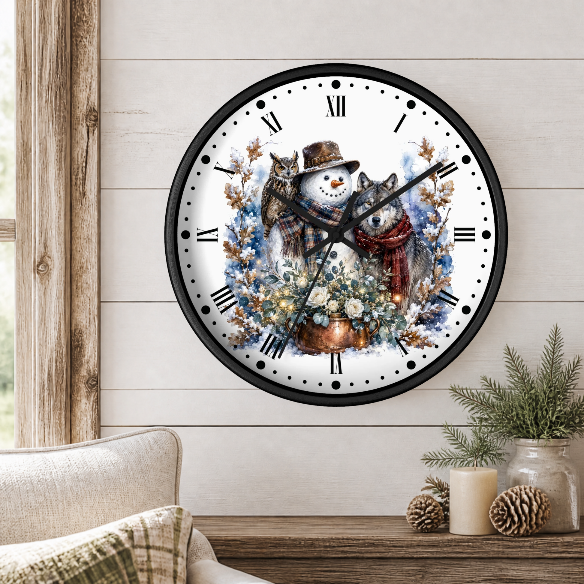 A round wall clock with a black frame and a winter illustration of a snowman, a wolf, and a owls among flowers, mounted on a light wood paneled wall above a table with candles and greenery.