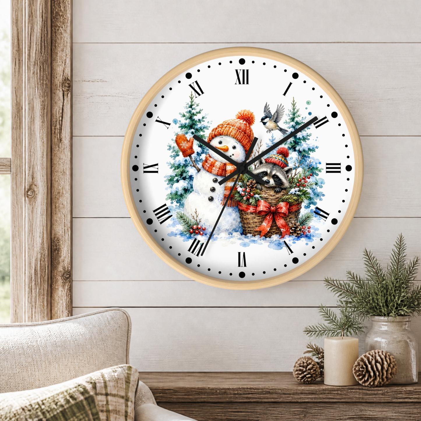 A round wall clock with a light wood frame hangs on a white shiplap wall above a wooden table. The clock face features a festive winter illustration with a snowman in an orange hat, a bird, a raccoon, and Christmas trees.