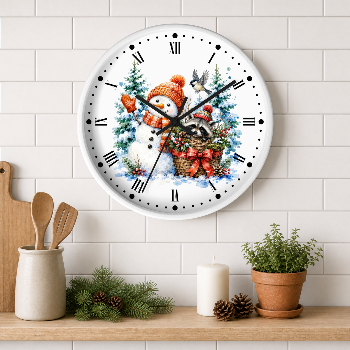 A round wall clock with a festive Christmas illustration featuring a snowman, raccoon, bird, and evergreen trees. The clock is mounted on a white subway tile wall above a wooden shelf styled with kitchen utensils, pinecones, a candle, and a potted plant.