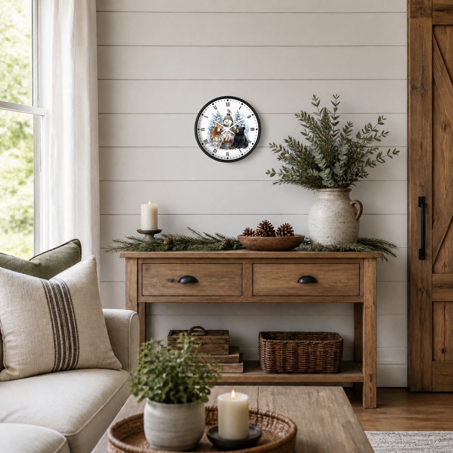 A round wall clock with a rustic holiday illustration of snowman, deer, bear, and bird, styled on a shiplap wall above a wooden console table in a cozy living room setting.