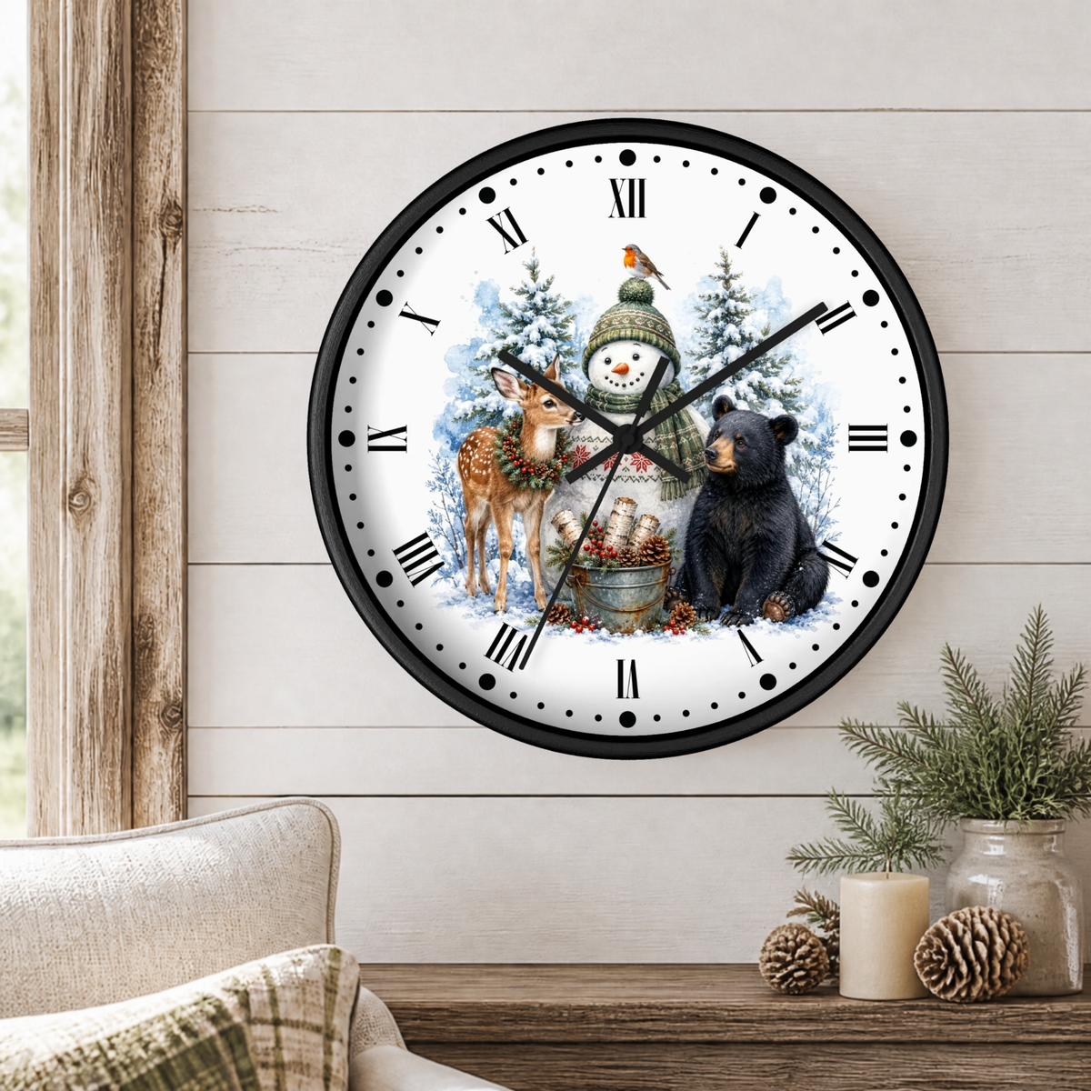 A round wall clock with a winter holiday illustration, featuring a snowman, deer, bear, and birds on a white face with black Roman numerals. The clock is mounted on a light wood-paneled wall above a rustic wooden table with a candle, pinecones, and a small plant.