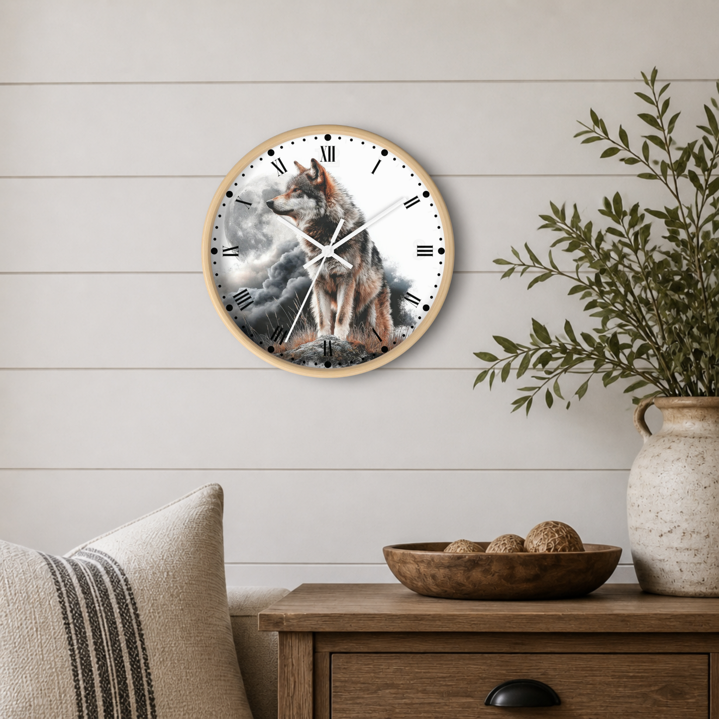 A round wall clock with a wolf illustration on the face, mounted on a white shiplap wall above a wooden side table with a plant and bowl.